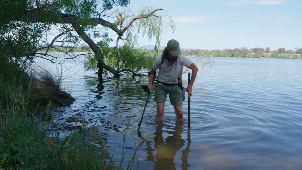 A woman with a metal detector, standing knee-deep in a river