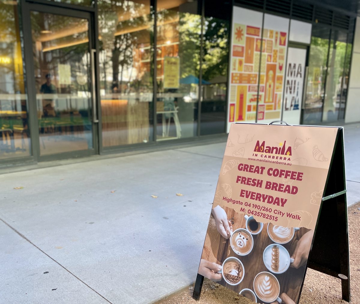 A frame sign with Manila in Canberra branding, and a photo of cups of coffee with the text 'great coffee, fresh bread, everyday'