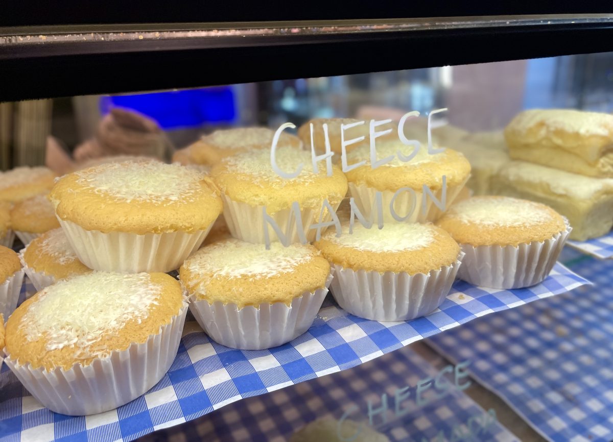 Cupcakes with shaved cheese on top in a cabinet. Text reading 'cheese mamon' has been written on the glass.