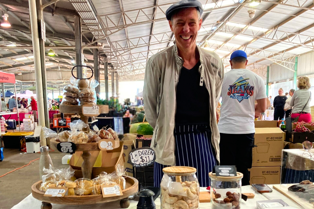 Man standing at market stalls with pastries.