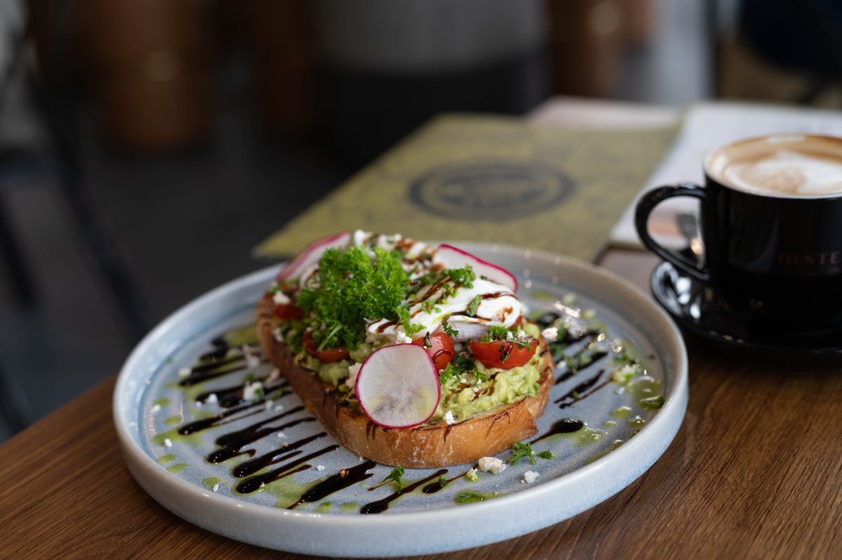 A plate of avocado- topped toast sits on a table near a coffee