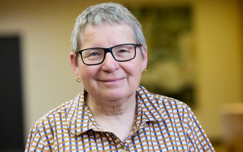 A short haired woman with glasses in a checkered shirt smiling at the camera