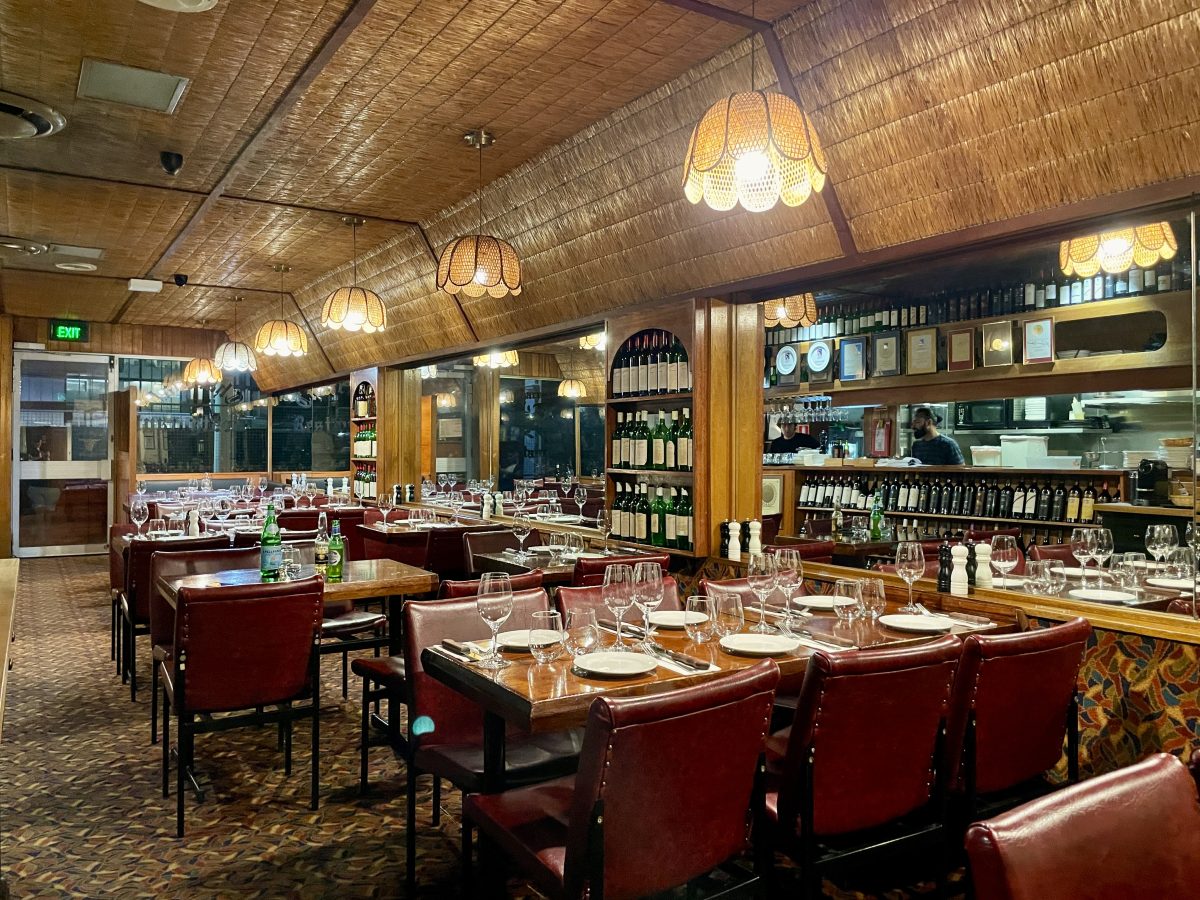 The interior of an old restaurant. There are leather seats, a colourful patterned carpet, textured reed-like ceiling, rattan lightshades and mirrors.
