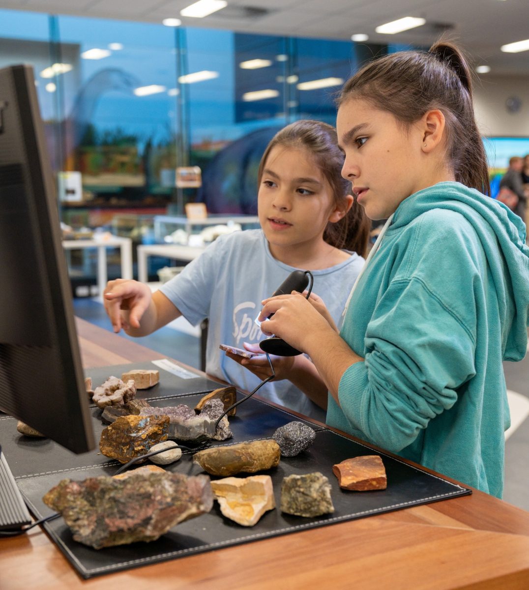 Two children use a microscope to examine rock specimens.
