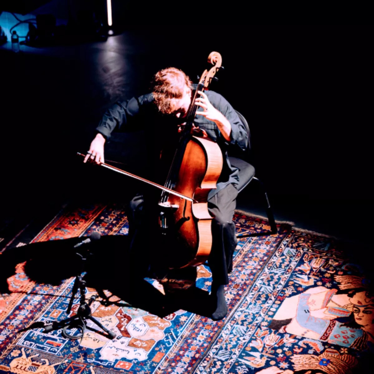 a spotlight on a person playing a cello on a colourful rug
