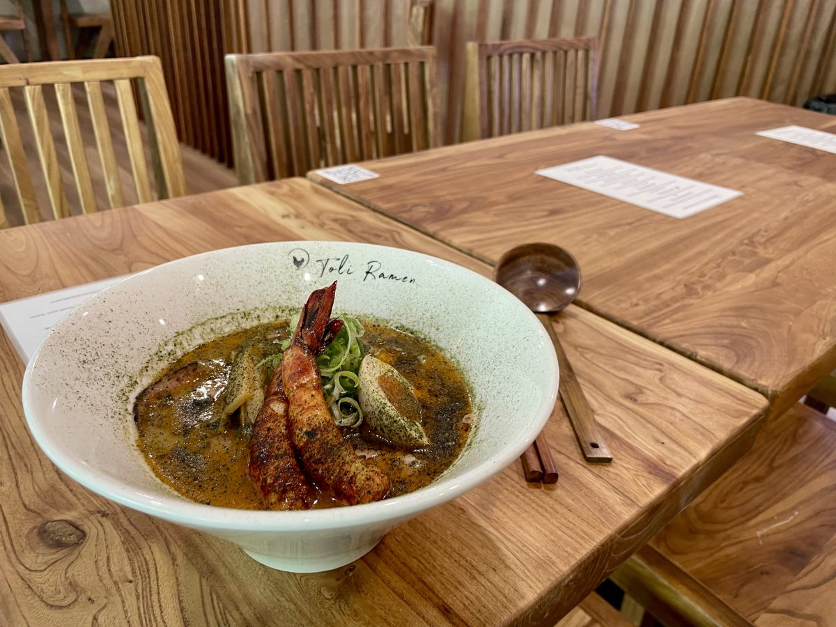 A bowl of ramen with two grilled prawns on top, and half an egg. 