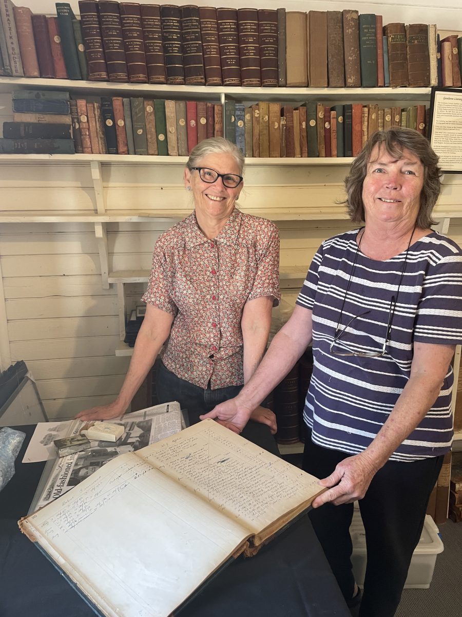 Two women holding a large ledger in front of a bookshelf