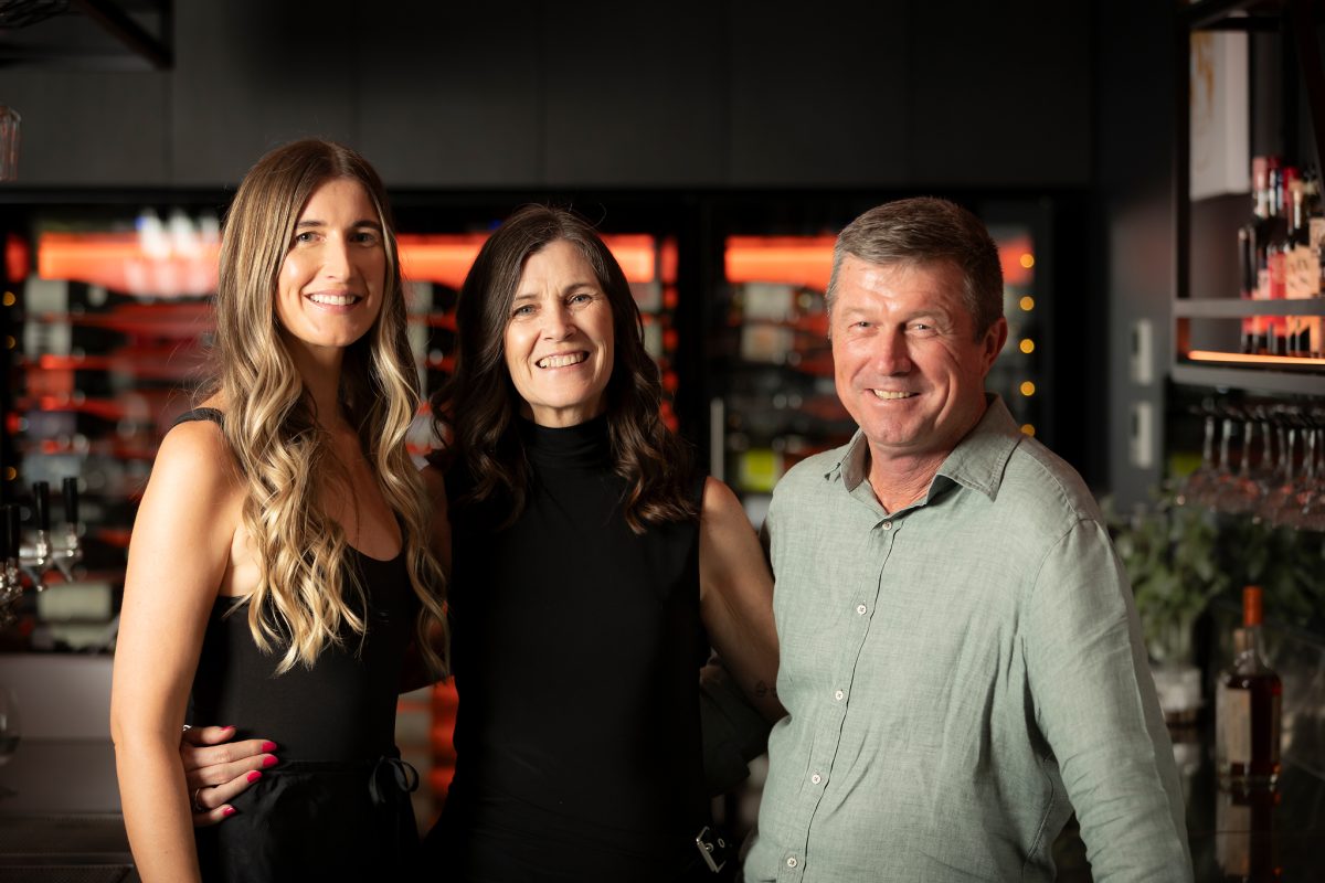 A family trio stands in a bar with arms around each other. 
